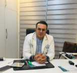 Doctor sitting at a desk in a professional office, wearing a white coat and looking at the camera.