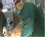 Surgeons wearing green scrubs and masks perform surgery in a hospital operating room.