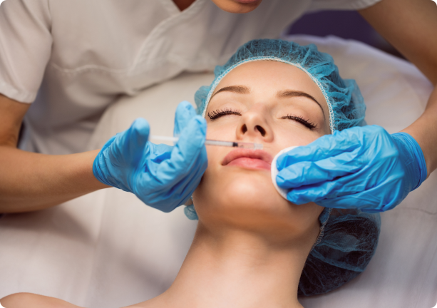 A woman wearing a blue hair cap receives a cosmetic injection in her lips by a gloved practitioner, conveying a clinical, focused atmosphere.