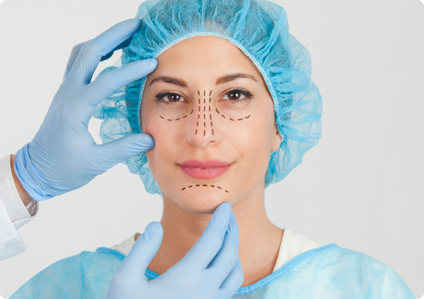 A person in medical attire with blue surgical cap and gown has dotted lines on face, indicating cosmetic procedure. Hands in gloves gently touch their face.